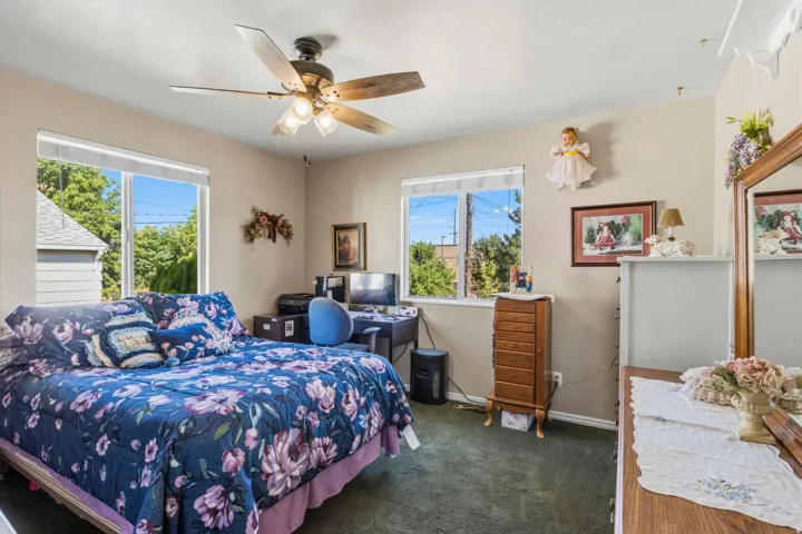 Bedroom featuring a ceiling fan with integrated lighting, two large windows, neutral wall tones, and green carpeting