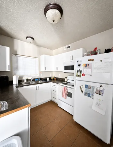Kitchen featuring white cabinetry, dark countertops, a double basin sink, and brown tile flooring