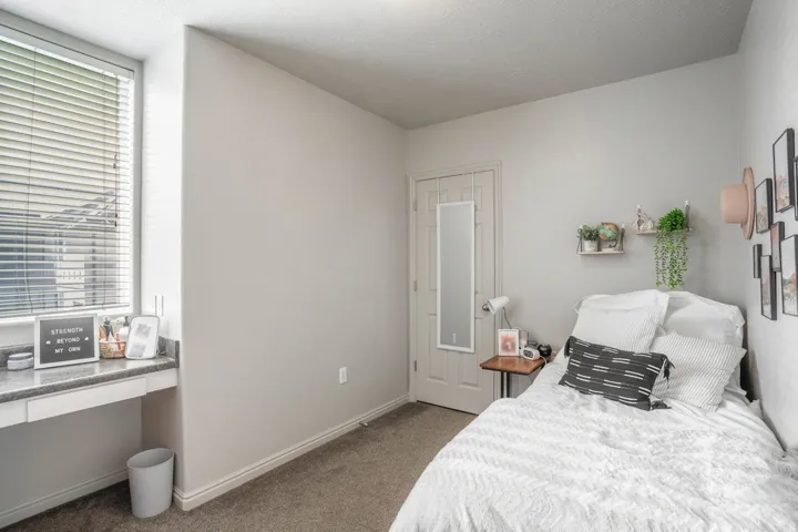 Room featuring a built-in desk with a dark flecked countertop, a window with horizontal blinds, a neutral-toned door, and carpet flooring