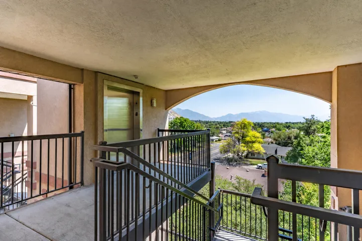 Outdoor walkway featuring a mountain backdrop, a residential area, metal railings, and an elevator access point