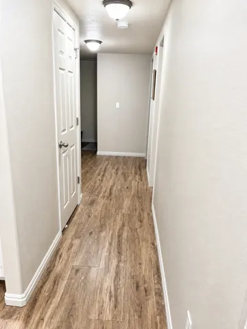 Hallway featuring wood-finish flooring, light neutral wall paint, and white trim molding