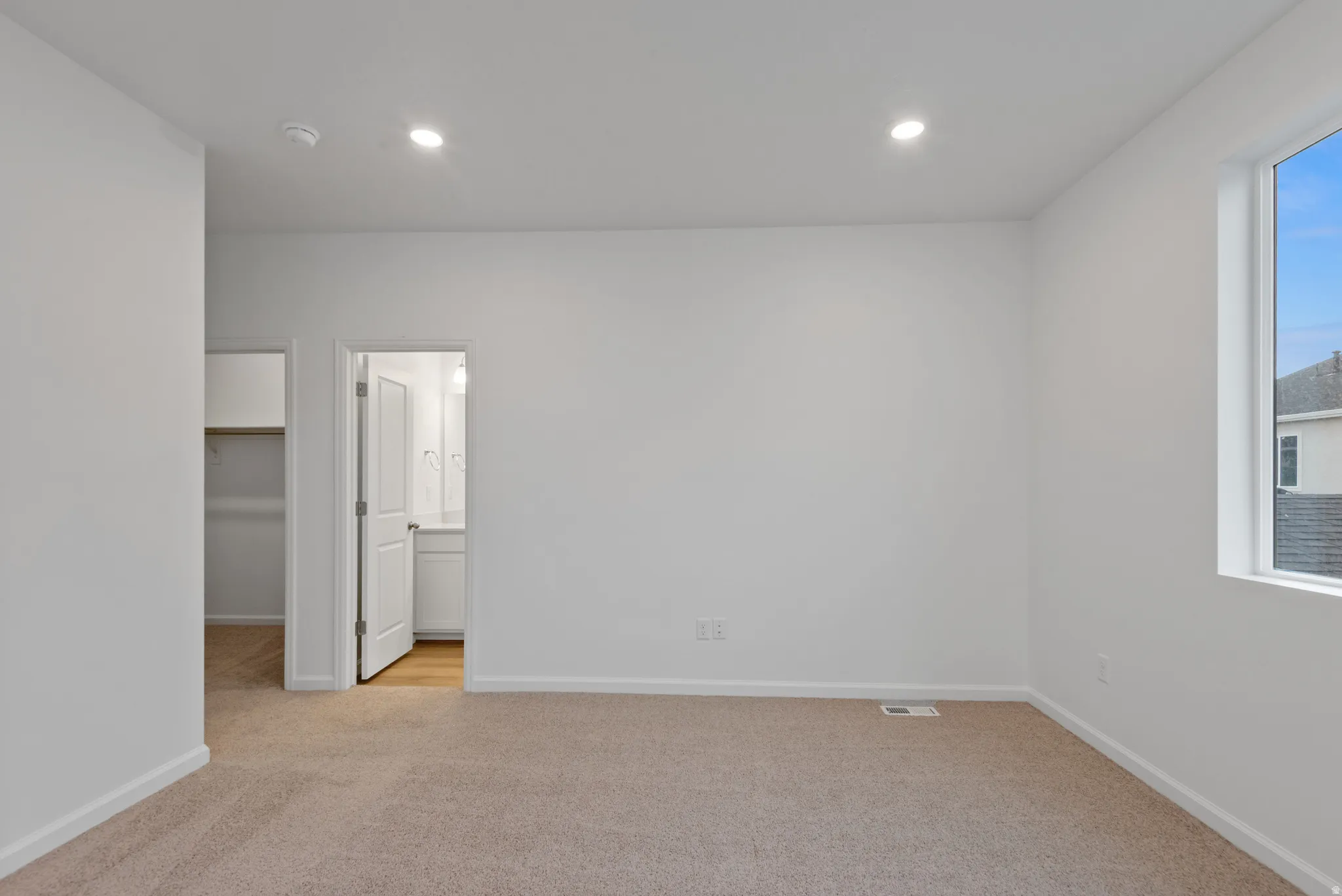Spacious room featuring neutral carpeting, recessed lighting, and a large window