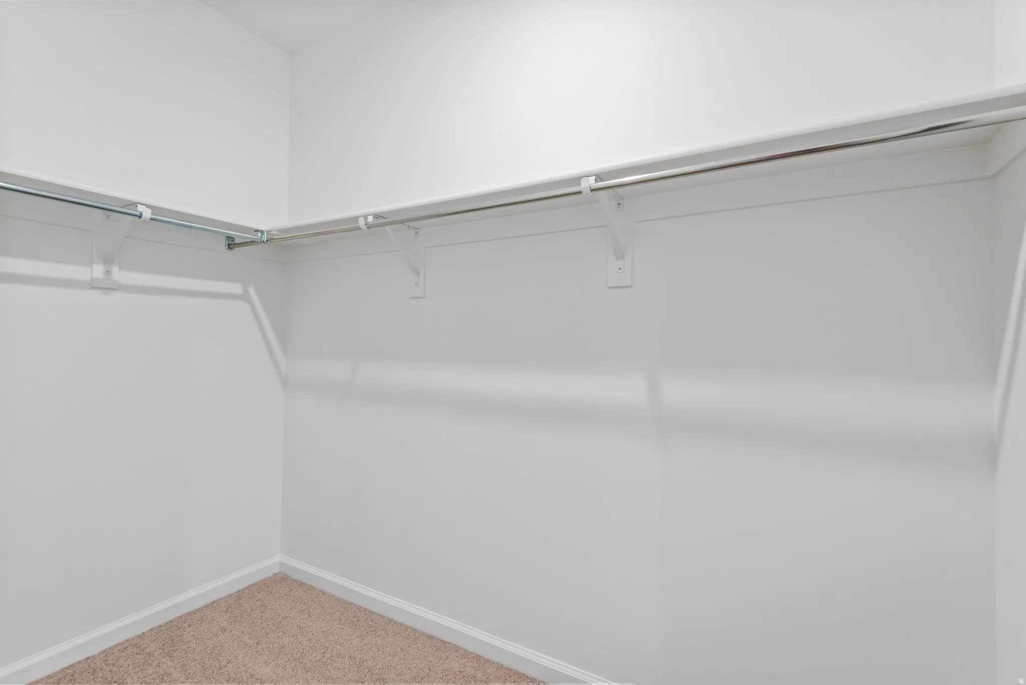 Walk-in closet featuring light-toned carpeting, white baseboards, and built-in shelving with hanging rods