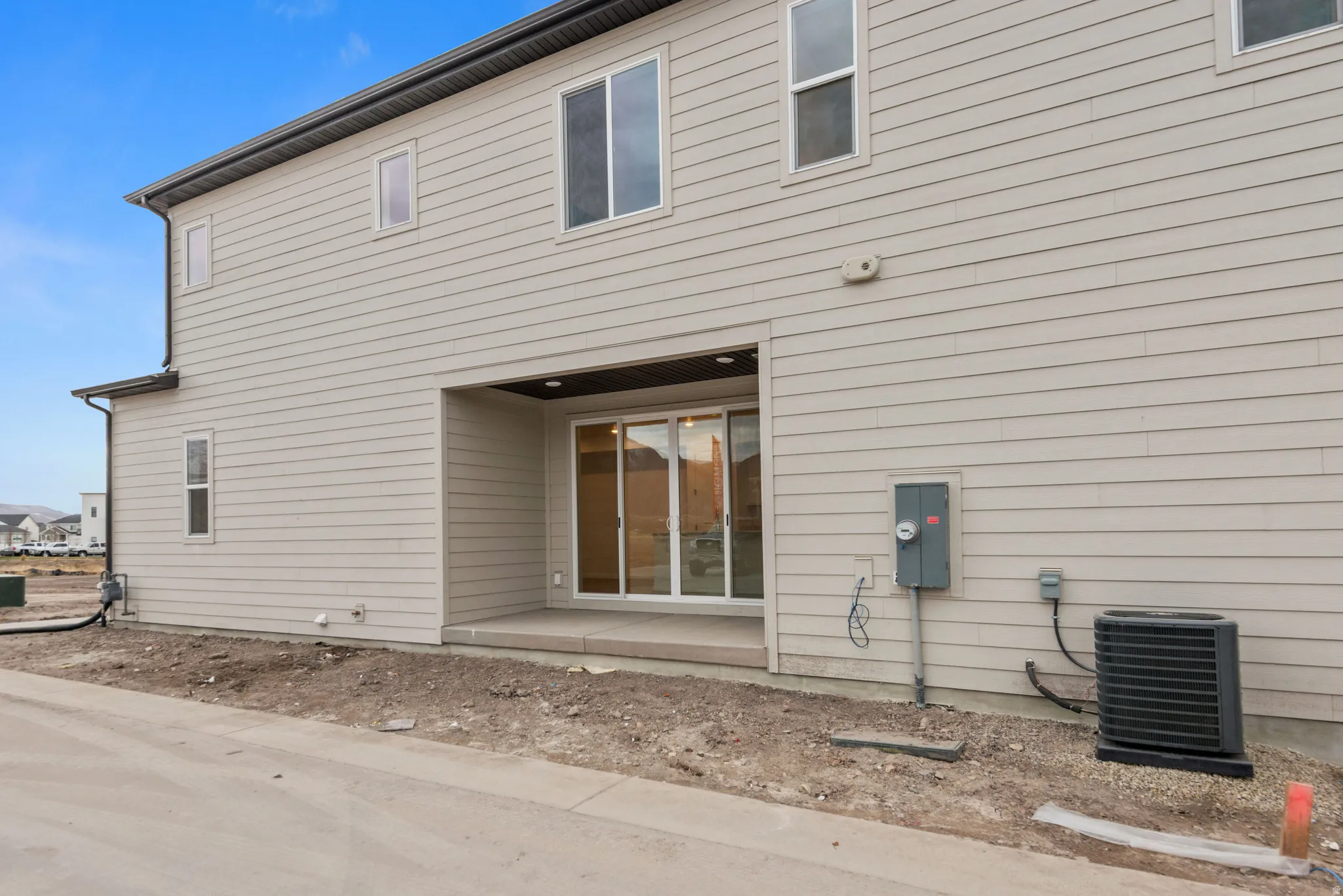 Two-story exterior with light-toned horizontal siding, multiple windows, and a covered patio area with sliding glass doors