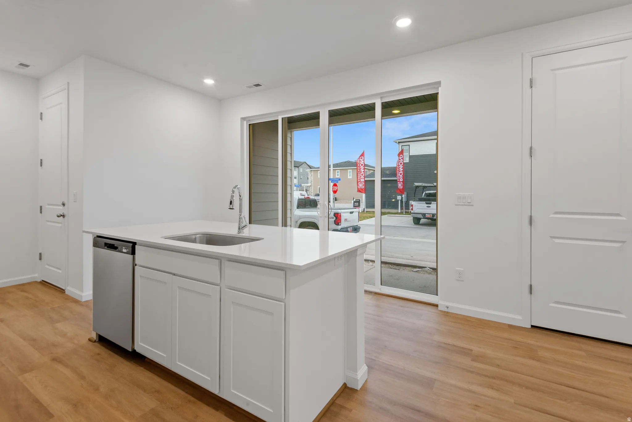 Kitchen island featuring a stainless steel sink with a high-arc faucet, integrated dishwasher, and white shaker-style cabinetry