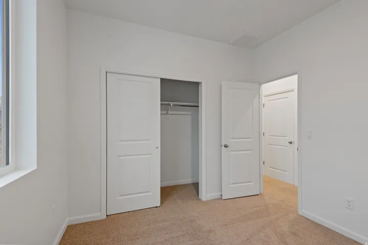 Room featuring light tan carpeting, white walls, a large window, a sliding closet door, and a standard white door