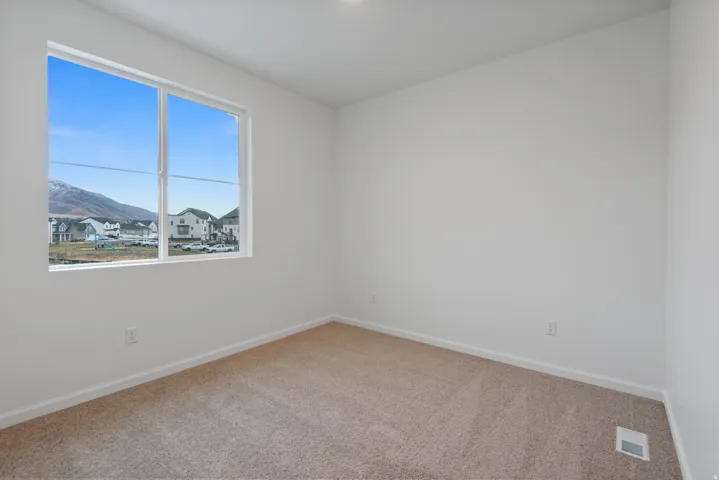 Light-filled room featuring a large window, neutral carpeting, white baseboards, and white walls
