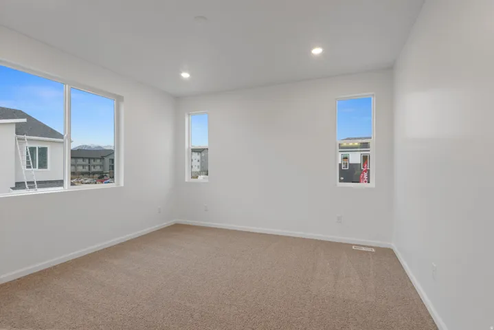 Spacious room featuring neutral carpeting, white walls, multiple windows, and recessed lighting