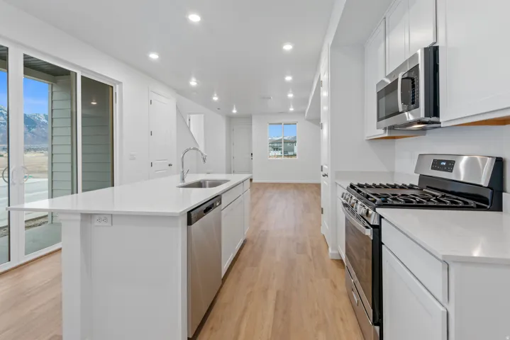 Contemporary kitchen featuring a spacious island with an integrated sink, stainless steel appliances, white cabinetry, and light-toned wood-finish flooring