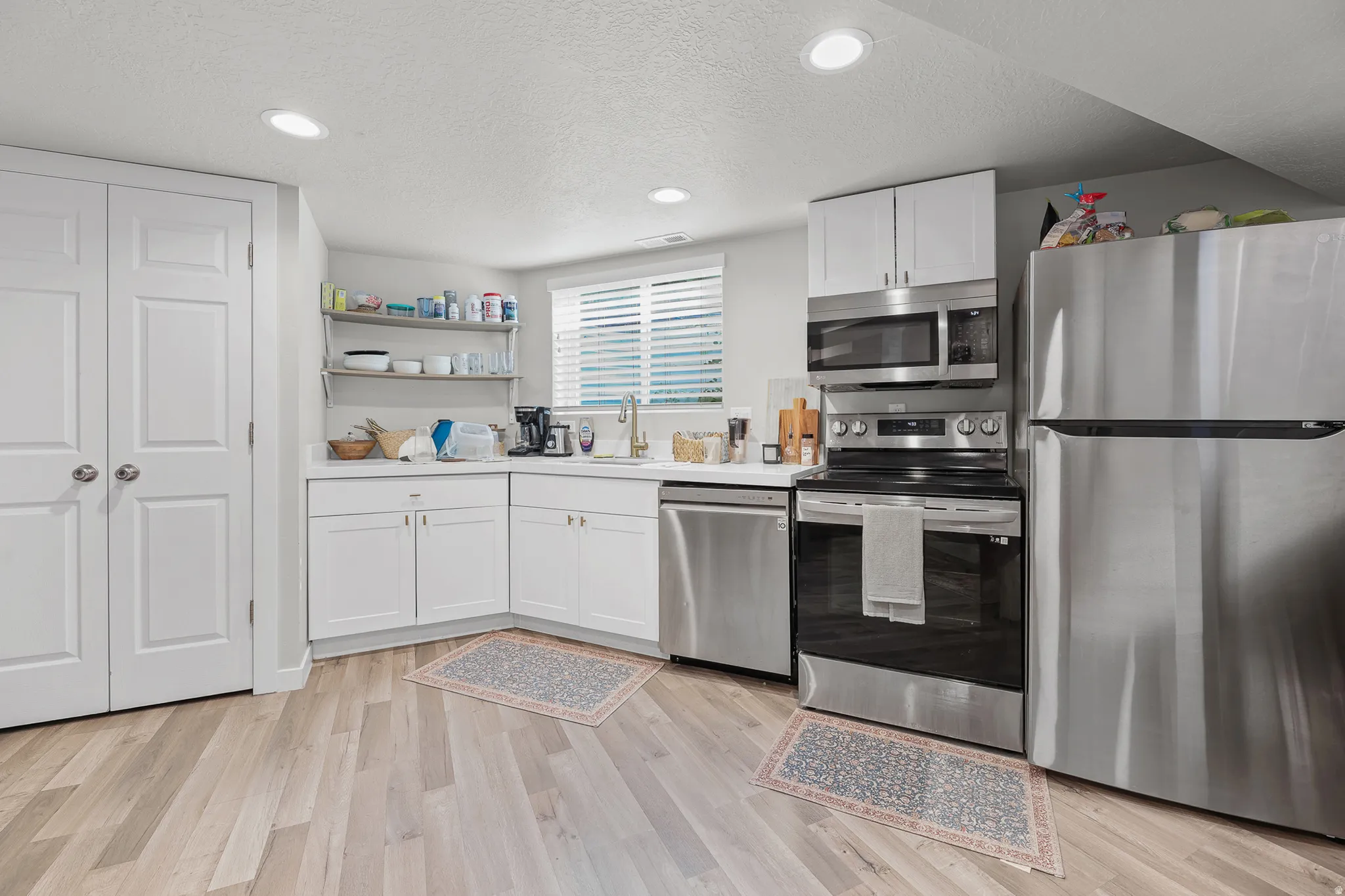Kitchenette featuring wood-finish flooring, white cabinetry, and stainless steel appliances including a refrigerator, range, microwave, and dishwasher