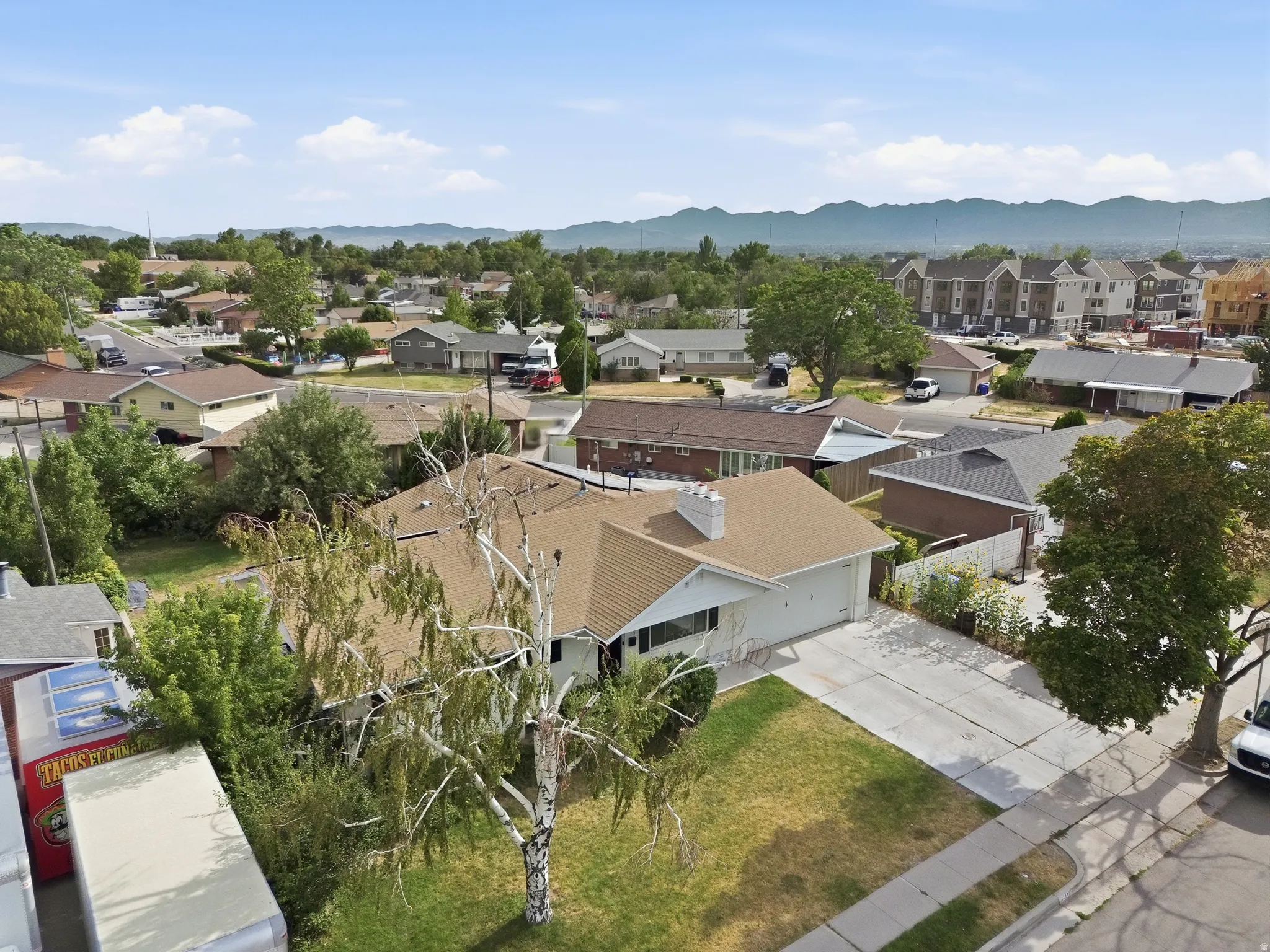 Ranch-style residence with an attached garage, featuring a paved driveway and a front lawn with mature trees