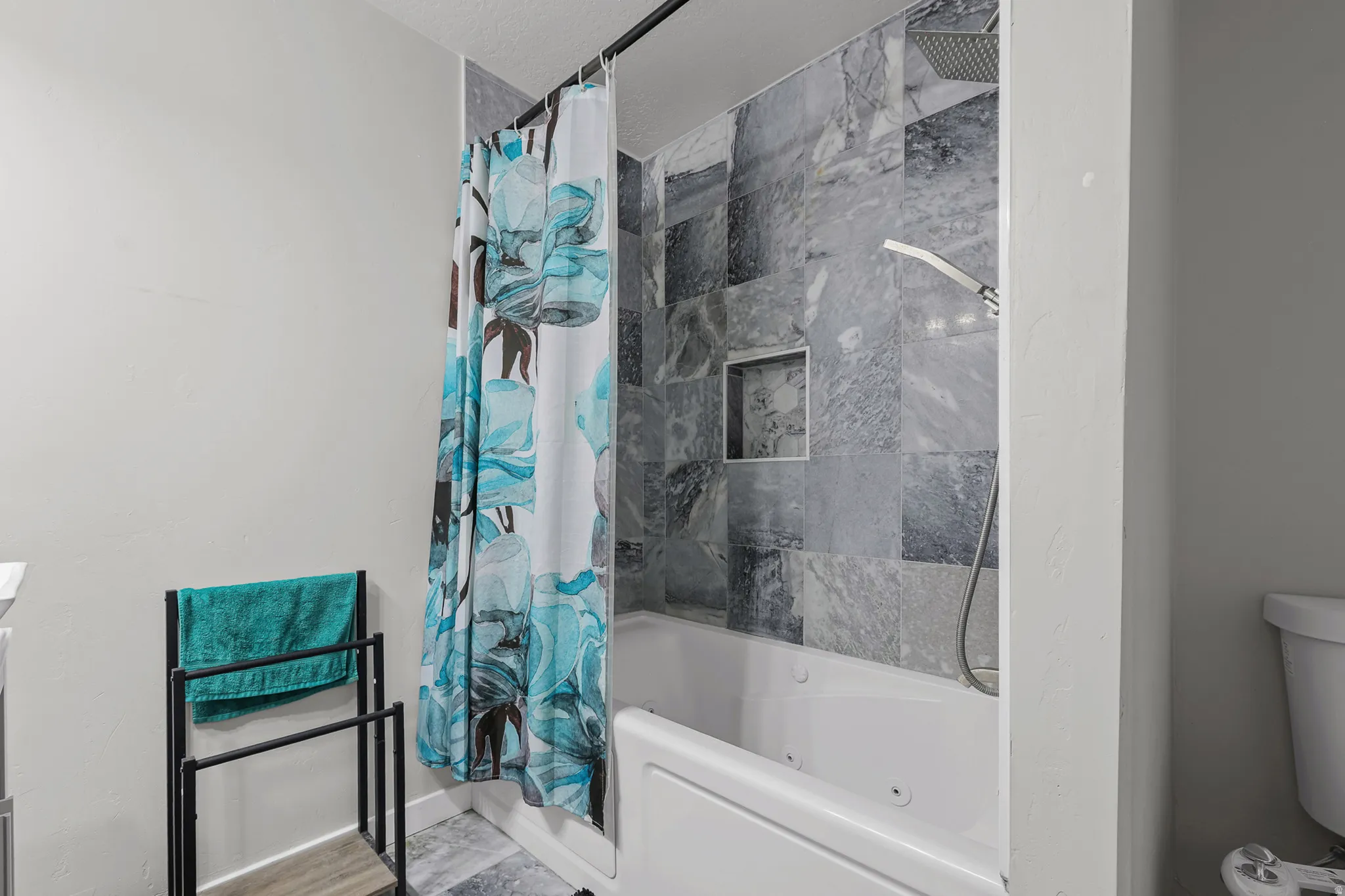Bathtub shower combination featuring multi-tone tile surround, recessed niche, and a rain shower head with a handheld sprayer