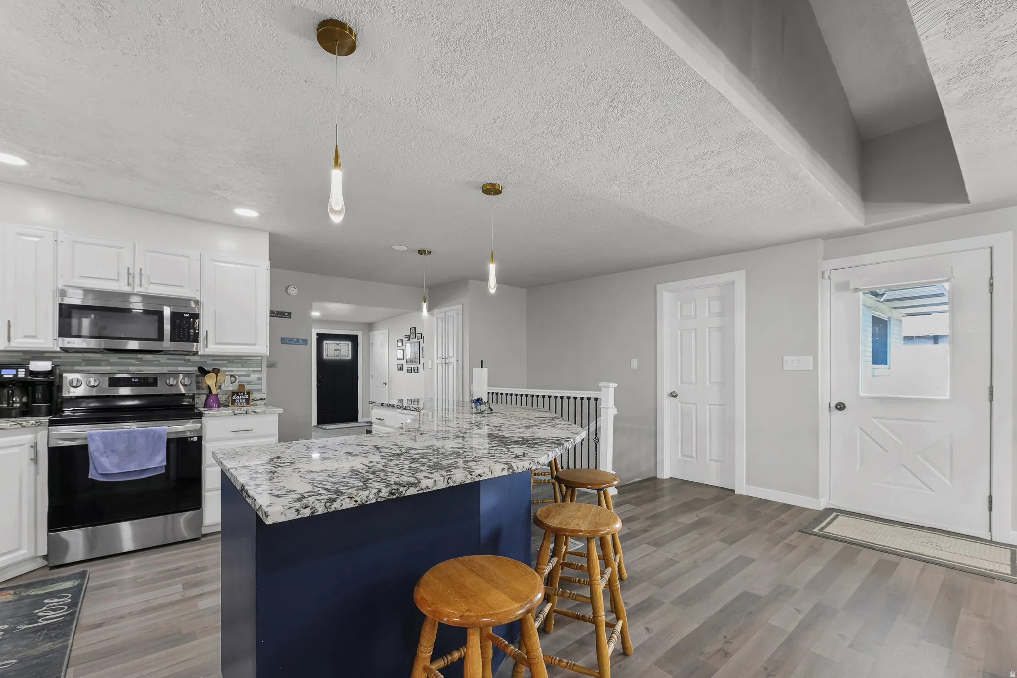 Kitchen featuring a granite-look island with a contrasting blue base, stainless steel appliances, and white cabinetry