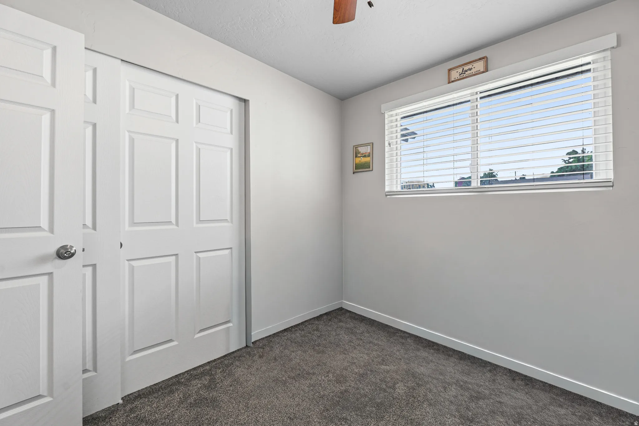 Room with gray carpet flooring, white walls, and a white-framed window featuring horizontal blinds