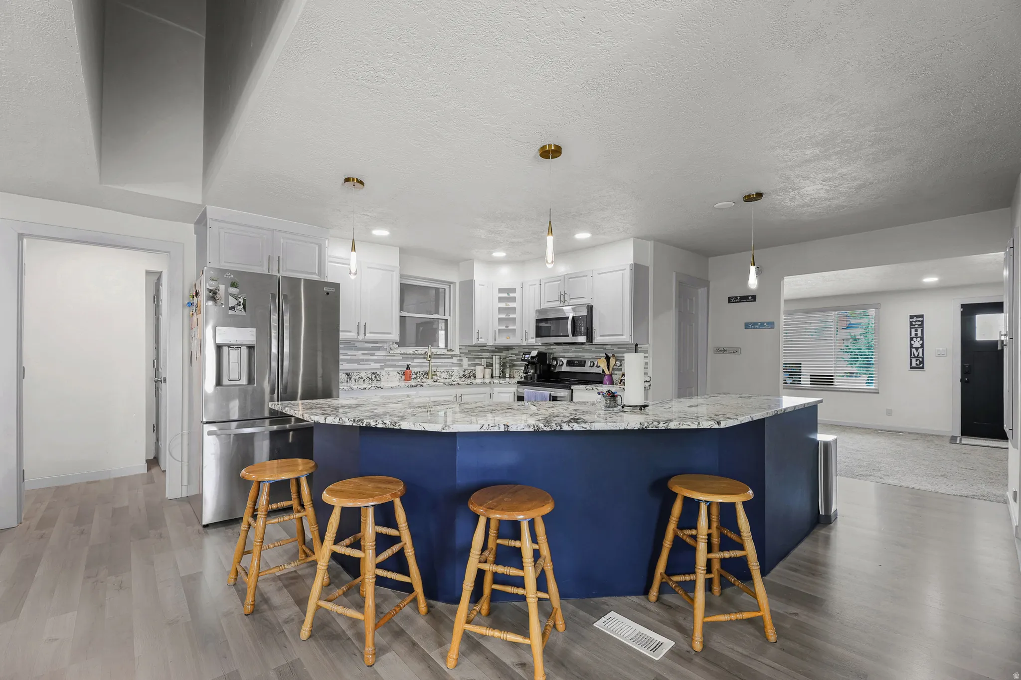 Kitchen featuring a blue island with seating, light gray wood-finish flooring, white cabinetry, a stainless steel refrigerator, and pendant lighting
