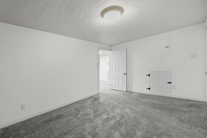Spacious room featuring freshly painted white walls, new gray carpeting, and a white six-panel door