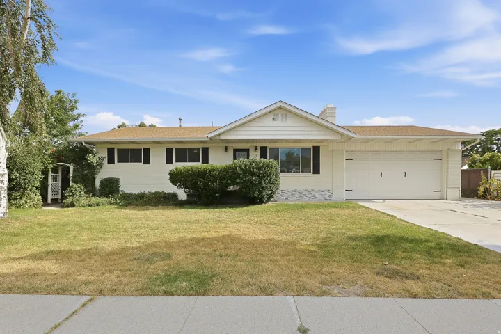 Ranch-style exterior with a two-car garage, concrete driveway, front lawn, and mature landscaping