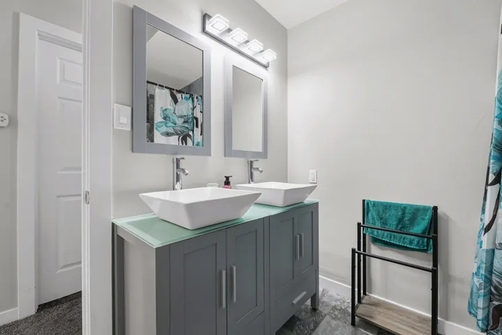 Dual vessel sinks with chrome faucets set on a contemporary vanity with a frosted glass countertop