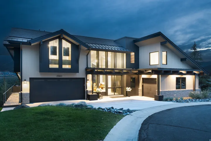 Modern architectural design featuring expansive windows, multiple garage bays, stone accents, and a winding driveway