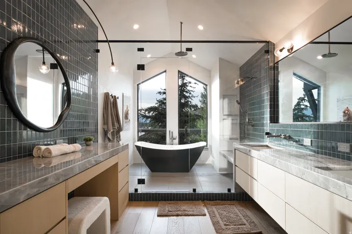Freestanding soaking tub with large picture windows, dual vanity with stone countertops, and a glass-enclosed shower with subway tile surround