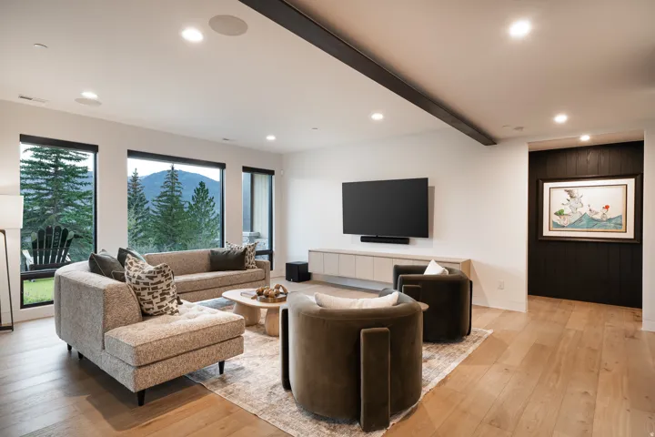 Recessed lighting, wood-finish flooring, custom built-in media console, dark wood paneled accent wall, and multiple windows with mountain and tree scenery