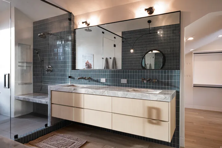 Double vanity with stone countertop, mounted faucets, and a full-width mirror