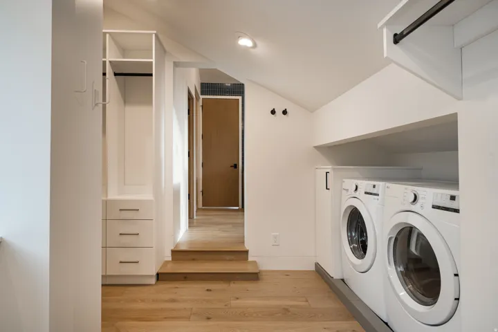 Integrated laundry area featuring two front-loading machines, built-in white cabinetry with drawers, and a hanging rod