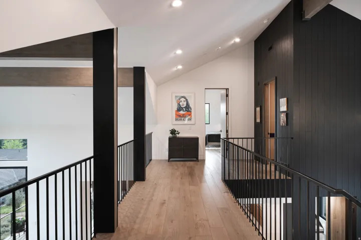 Vaulted ceiling with recessed lighting, wood-finish flooring, dark wood accent wall, black metal railings, and exposed structural beams