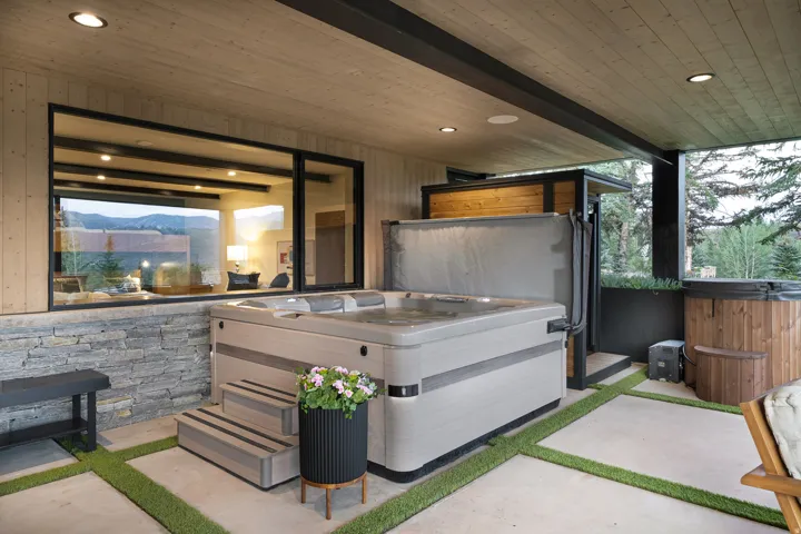 Covered outdoor spa area with a stone veneer wall, concrete patio, and integrated artificial turf accents