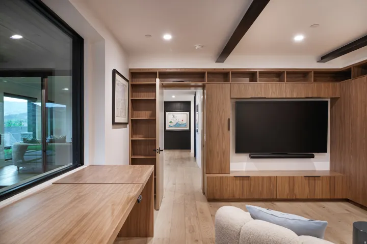 Built-in wood-finish shelving, an integrated entertainment center, wood-finish flooring, a wood-finish desk, and a large sliding glass panel
