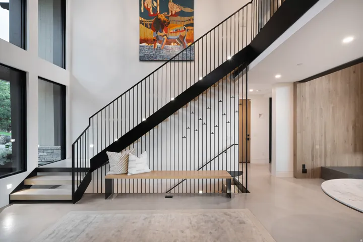 Floating staircase with black metal railings, tall windows, light wood-finish wall paneling, recessed lighting, and light-toned flooring