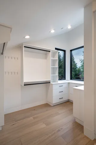 Light wood-finish flooring, white built-in cabinetry with black hardware, recessed lighting, and corner windows