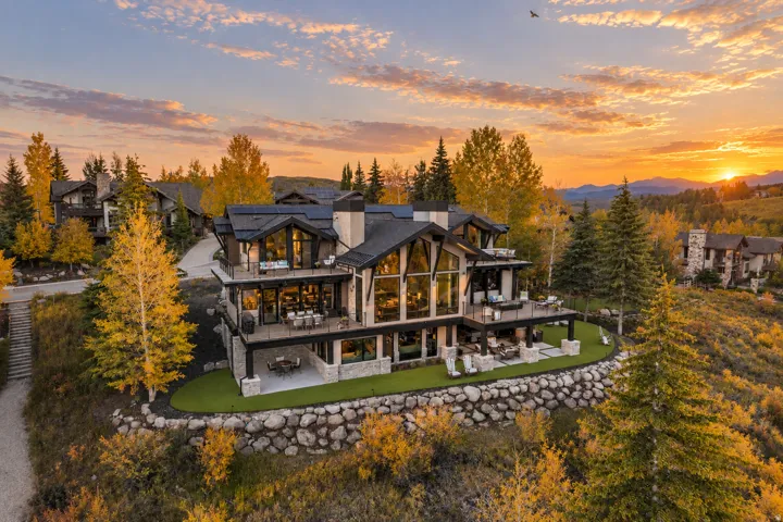 Multi-level architectural design with extensive window walls, multiple balconies and patios, and a stone retaining wall