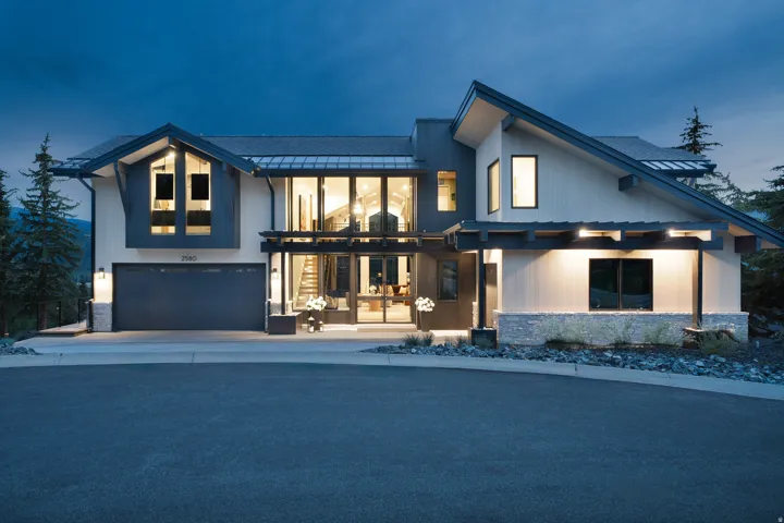 Modern architectural design with a dark gray garage door, stone accents, and expansive window placements