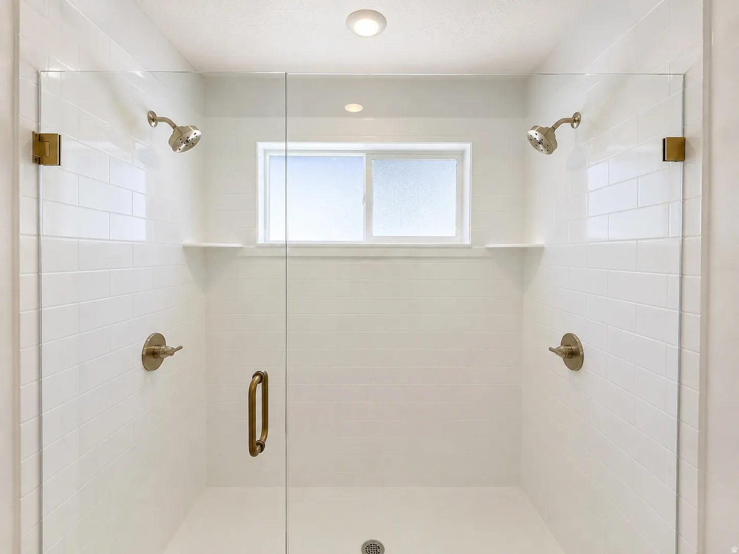Spacious shower enclosure with clear glass panels, dual showerheads, subway tile surround, built-in shelving, and an integrated window