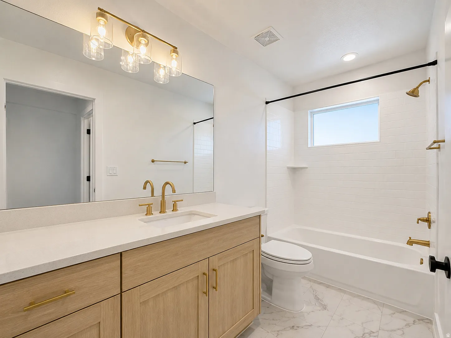 Modern bathroom featuring a wood-finish vanity with a light-toned countertop, a rectangular undermount sink, and brass-finish fixtures