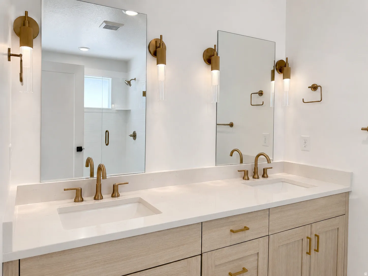 Double vanity featuring light wood-finish cabinetry, white countertop, and dual undermount sinks with brass fixtures