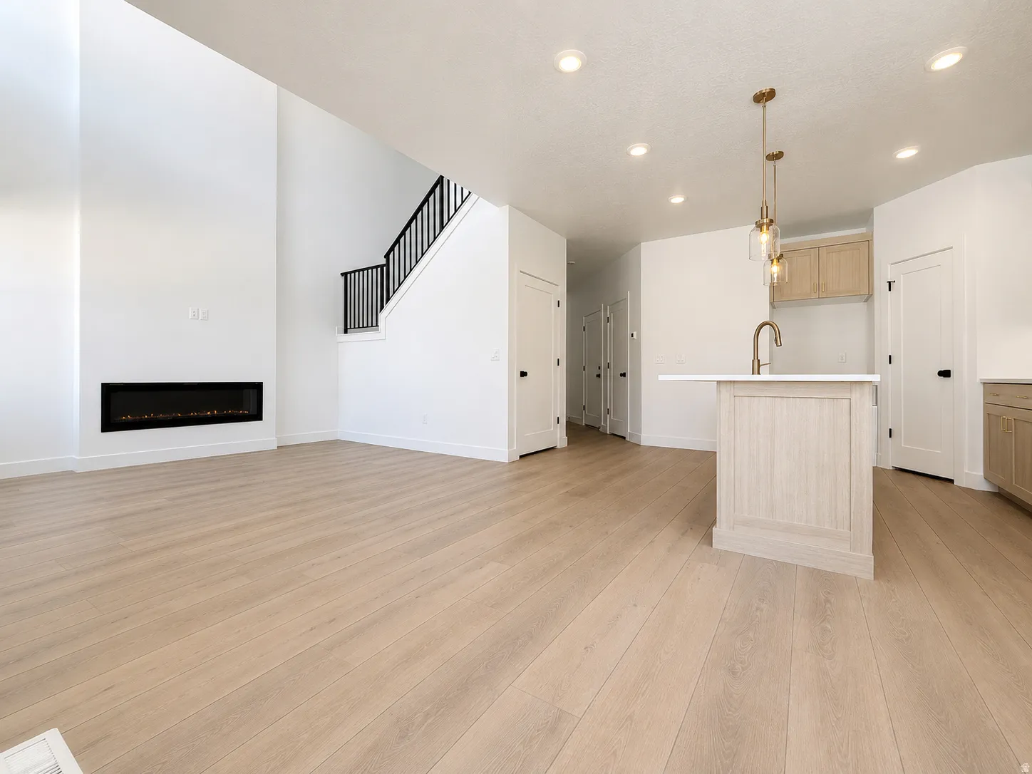 Open-concept living space featuring light wood-finish flooring, a linear electric fireplace, and a two-story ceiling