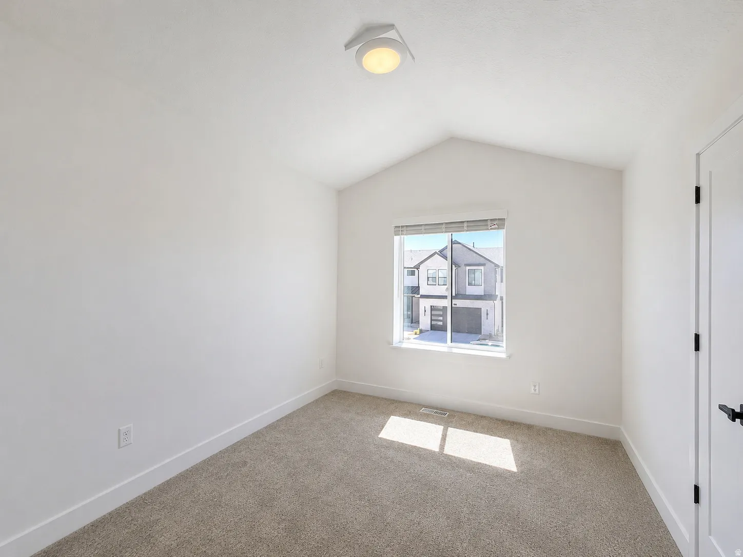 Carpeted room featuring a vaulted ceiling and a rectangular window