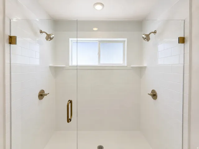 Spacious shower enclosure with clear glass panels, dual showerheads, subway tile surround, built-in shelving, and an integrated window