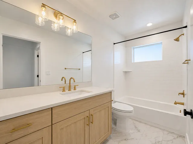 Modern bathroom featuring a wood-finish vanity with a light-toned countertop, a rectangular undermount sink, and brass-finish fixtures