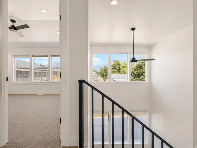 Two-story interior featuring a black metal handrail, multiple windows, recessed ceiling lighting, and two ceiling fans