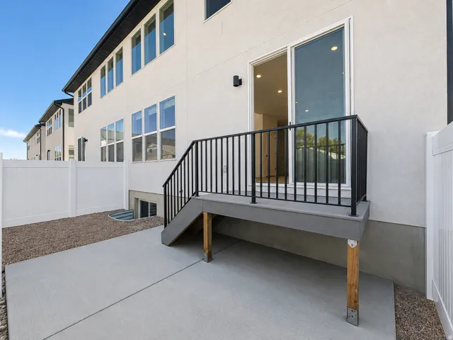 Rear exterior showcasing a concrete patio, composite deck with black railings, and a sliding glass door