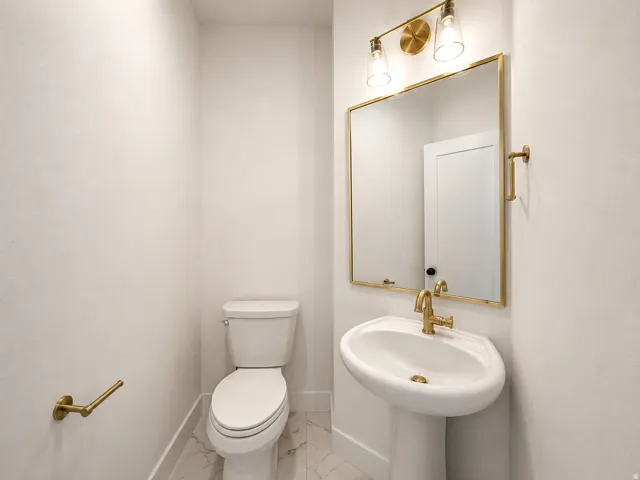 Pedestal sink with brass-finish faucet, rectangular mirror with brass-finish frame, two-light brass-finish vanity fixture, and white porcelain toilet