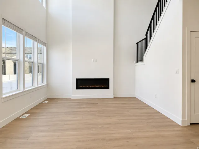 Two-story living area featuring a linear electric fireplace, wood-finish flooring, and a bank of windows