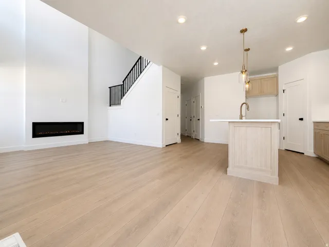 Open-concept living space featuring light wood-finish flooring, a linear electric fireplace, and a two-story ceiling