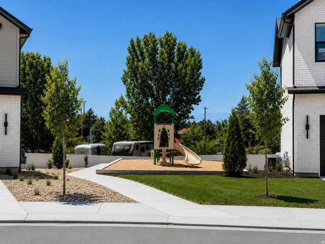 Community play structure with slide feature, surrounded by mature trees and manicured lawn