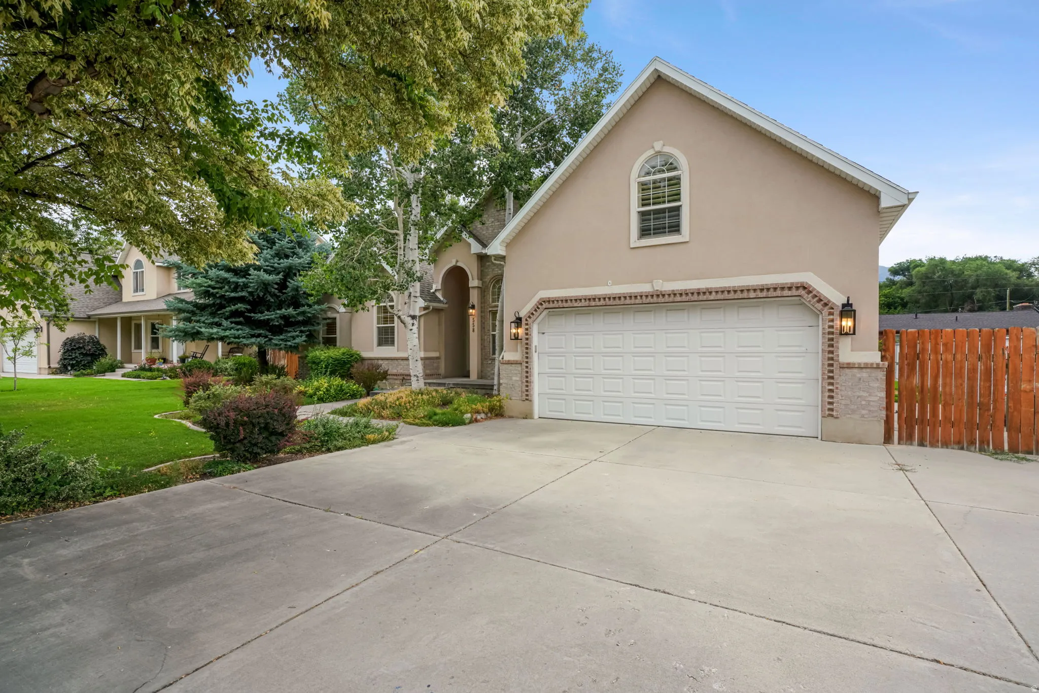 Exterior featuring a light stucco finish, a two-car garage with an arched window above, brick detailing, and a concrete driveway
