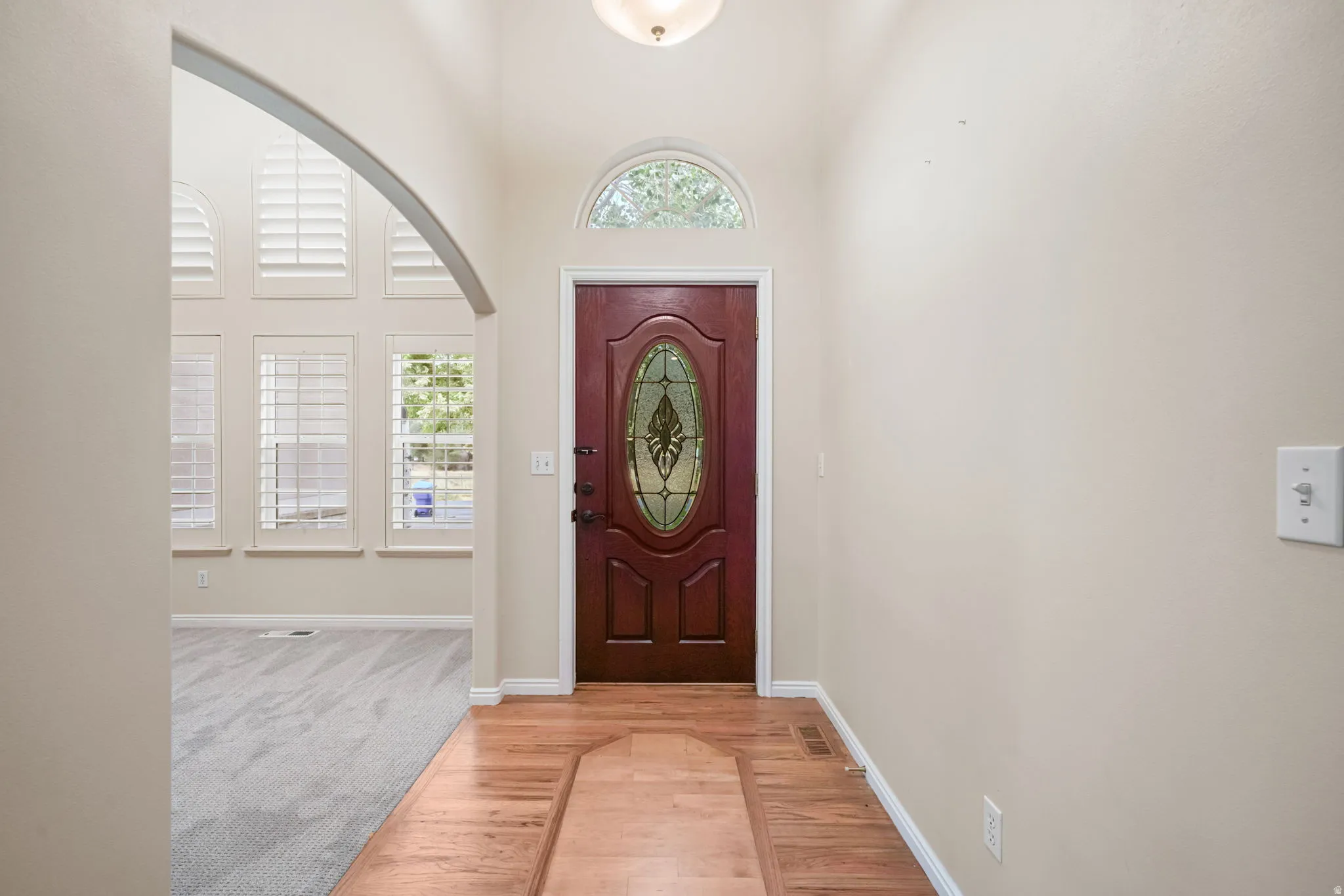 Wood-finish flooring entry with a decorative oval glass front door and arched transom window