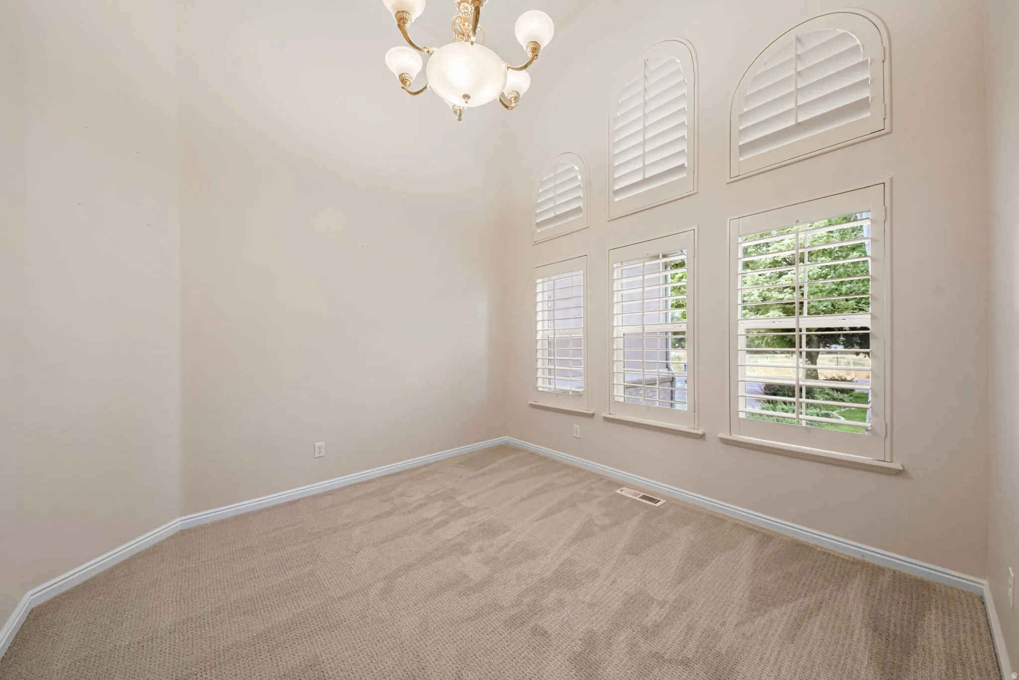 Room featuring vaulted ceilings, carpet flooring, a multi-pane window configuration with arched upper windows, white louvered plantation shutters, and an ornate ceiling-mounted light fixture